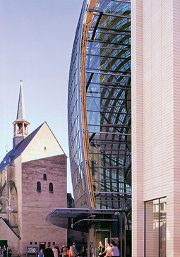 Köln Konstrukcija od drvenih upregnutih nosača otvara se visokim četverokatnim prostorom prema jedinstvenoj gotičkoj katedrali i romaničkoj crkvi. Takt i ritam gotike prenesen je u suvremenu i nekompromisnu vertikalnu strukturu