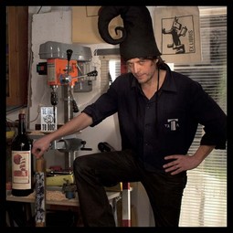 Habjan u radionici s vilenjačkom kapom, predmetom iz Dućana, i bocom hvarskog crnog vina s etiketom Petikat